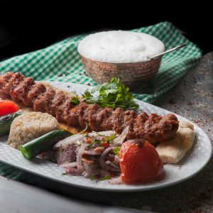 From above adana kebab with rice and fried vegetables and chopped onion and ayran in white plate on stone background