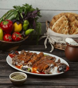 iskender kebab garnished with tomato sauce and yoghurt, served with grilled vegetables