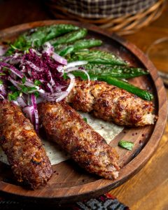 side view of lula kebab with red onions  sumakh and grilled green chili peppers on a wooden board